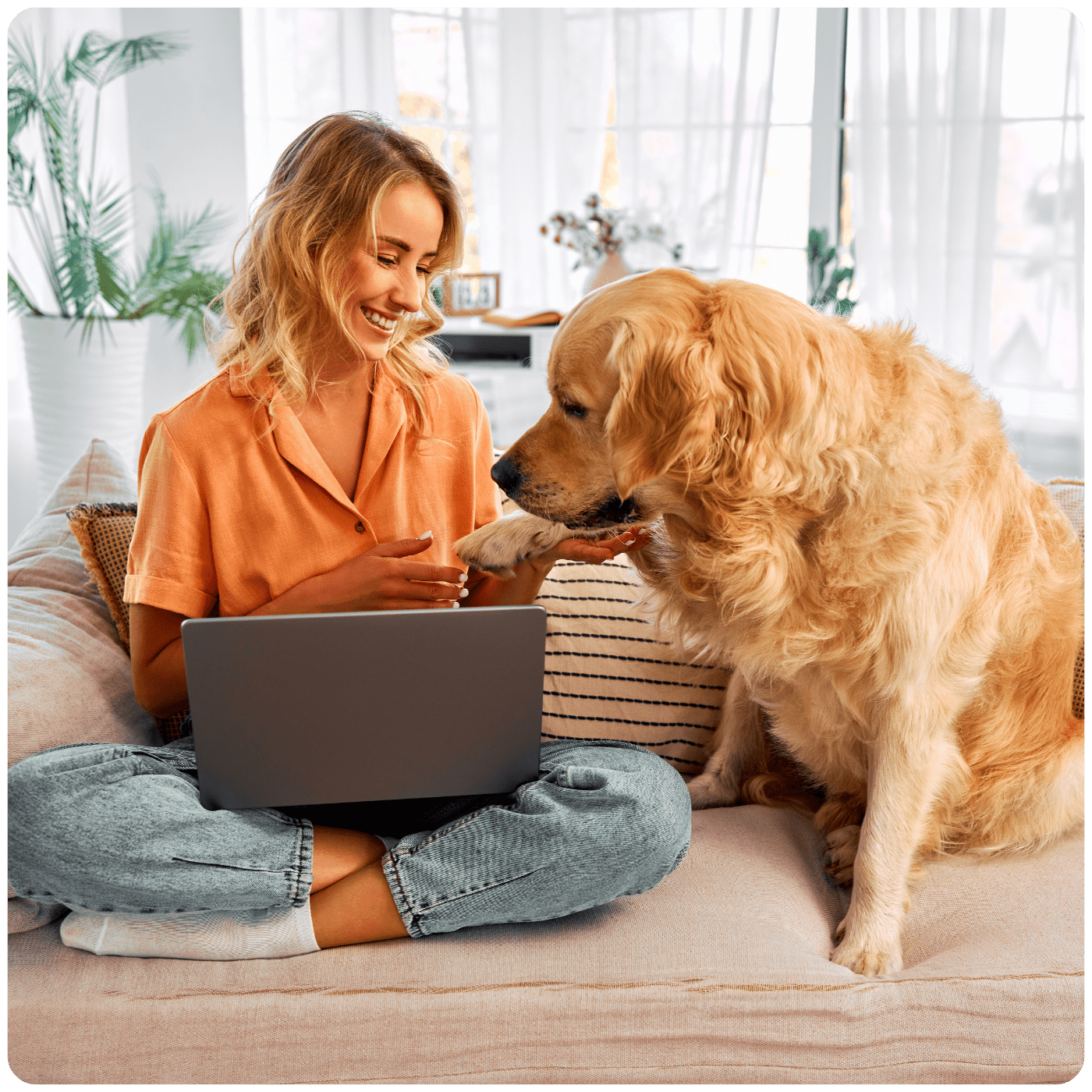 Woman sat on the sofa using her laptop whilst dog sits next to her