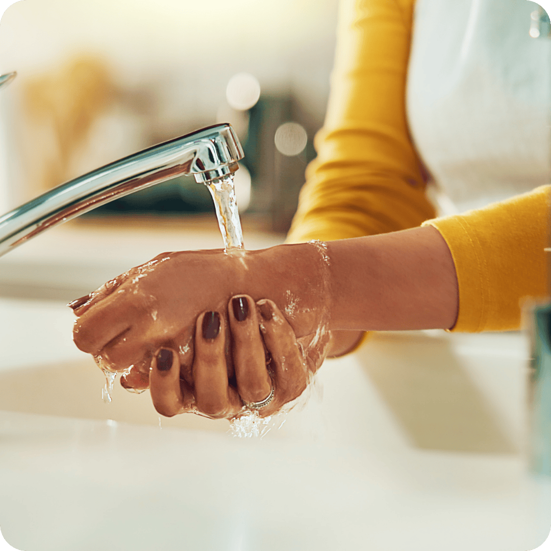 Person washing hands under a running faucet with a blurred background